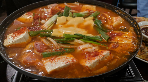 A bubbling pot of spicy stew with tofu, green onions, and seasonings, served in a black pot.