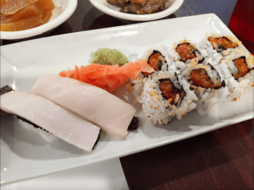 A plate of sushi featuring two pieces of sashimi, a roll with eel, wasabi, and pickled ginger.