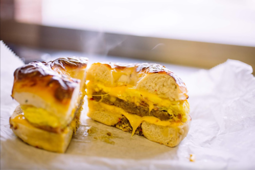A freshly cut sandwich with melted cheese, egg, and a savory patty, emitting steam, on parchment paper.