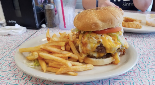 A large cheeseburger with lettuce, tomato, and melted cheese, served with a side of golden French fries.