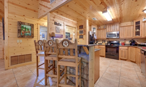 Cozy wooden kitchen with bar stools, stone accents, and rustic decor, featuring modern appliances and warm lighting.