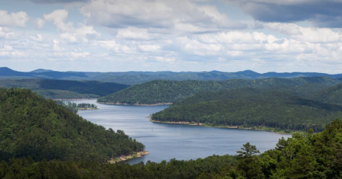 A scenic view of a winding river surrounded by lush green hills and mountains under a partly cloudy sky.