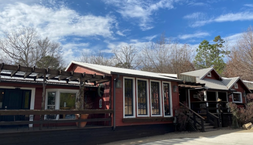 A red wooden building with large windows, surrounded by trees and a blue sky with clouds.