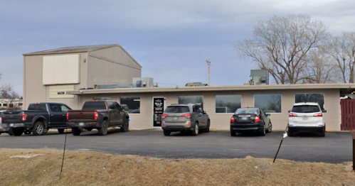 A small commercial building with several parked cars in front, set against a cloudy sky.
