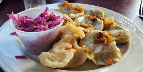 A plate of dumplings topped with sautéed onions, served with a side of purple cabbage slaw.