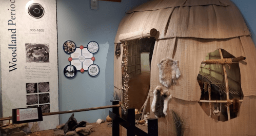 A replica of a Woodland Period dwelling with informational displays about the era, featuring natural materials and artifacts.