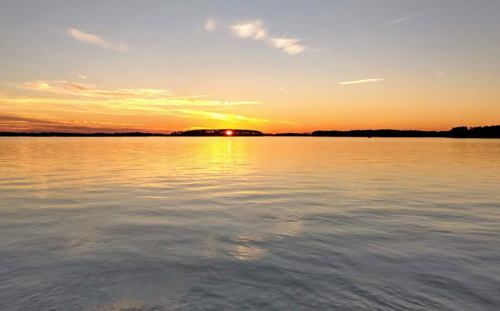 A serene sunset over calm water, with vibrant orange and yellow hues reflecting on the surface.