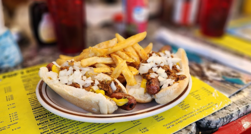 Two hot dogs topped with onions and mustard, served with a side of golden French fries on a colorful menu background.