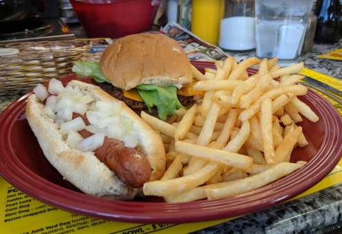 A plate with a hot dog topped with onions, a burger with lettuce, and a side of fries.