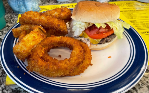 A plate with a cheeseburger topped with lettuce and tomato, alongside crispy onion rings and fried pickles.