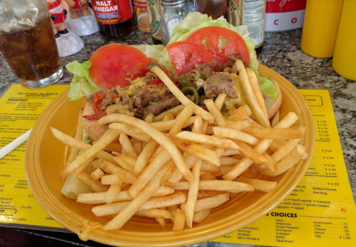 A plate with a sandwich topped with lettuce, tomatoes, and meat, served with a generous side of fries.