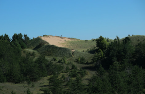 A sandy hilltop surrounded by green vegetation and trees under a clear blue sky.
