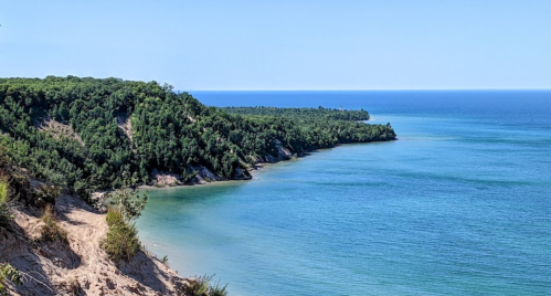 A serene coastal view featuring lush green cliffs meeting a calm blue lake under a clear sky.