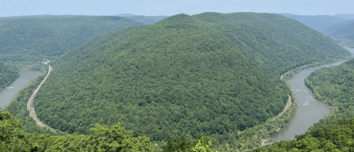A panoramic view of lush green mountains surrounding a winding river under a clear blue sky.