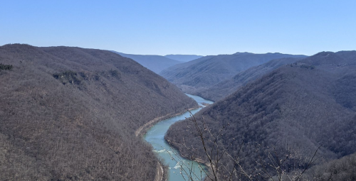 A winding river flows through a valley surrounded by bare, rolling mountains under a clear blue sky.