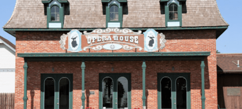 Historic brick building with a decorative sign reading "Opera House" and green trim, featuring large arched windows.