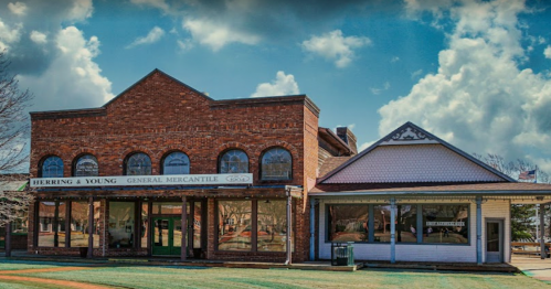 Historic brick general mercantile building with large windows, set against a cloudy blue sky.