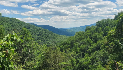 Lush green mountains stretch into the distance under a partly cloudy sky, showcasing a serene natural landscape.