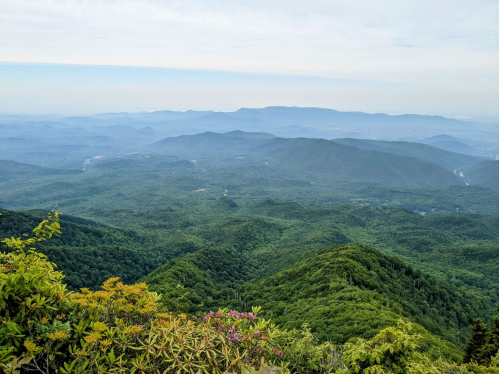 A panoramic view of lush green mountains and valleys under a cloudy sky, showcasing layers of distant hills.