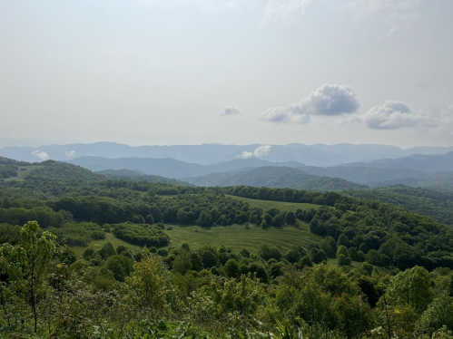 A panoramic view of rolling green hills and mountains under a cloudy sky.