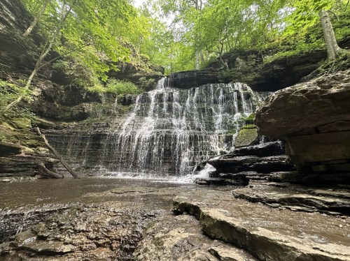 A serene waterfall cascading over rocky cliffs, surrounded by lush green trees and a tranquil pool below.