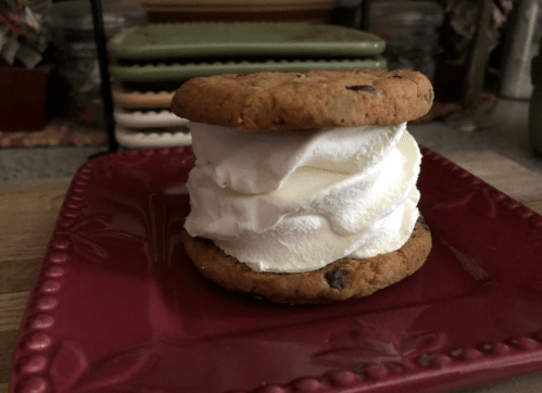A cookie sandwich with chocolate chip cookies and a thick layer of vanilla ice cream, served on a red plate.