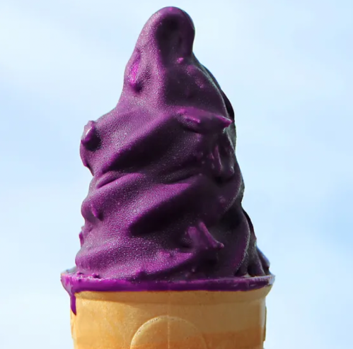 A close-up of a purple soft-serve ice cream cone against a light blue background.