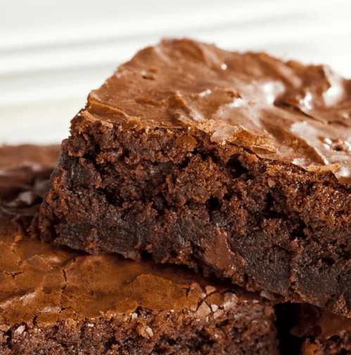 Close-up of rich, fudgy brownies with a shiny, cracked top and a soft, gooey interior.