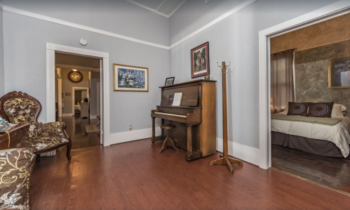 A cozy room featuring a vintage piano, a decorative chair, and an adjoining bedroom visible in the background.
