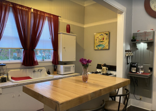 Cozy kitchen with a wooden table, red curtains, and modern appliances, featuring a sink and a small coffee station.