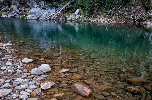 A serene river with clear, turquoise water and rocky banks, surrounded by lush greenery and trees.