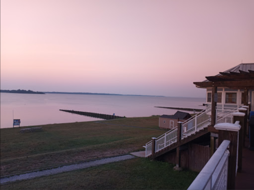 A serene waterfront view at dusk, featuring calm waters and a gentle pink sky. A pier extends into the distance.