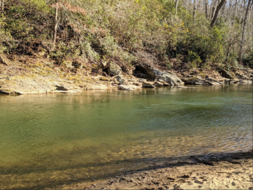 A serene river flows gently between rocky banks, surrounded by trees and greenery.