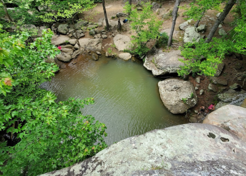 A serene pond surrounded by rocks and lush greenery, viewed from above.