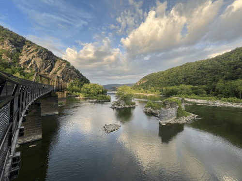 A scenic view of a river surrounded by lush hills, with a bridge on the left and rocky islands in the water.