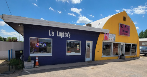 Exterior view of La Lupita's restaurant, a purple building with an "Open" sign, next to a yellow repair shop.