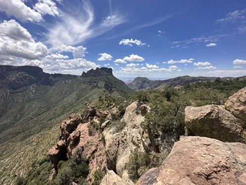 A panoramic view of rugged mountains and rocky terrain under a bright blue sky with scattered clouds.