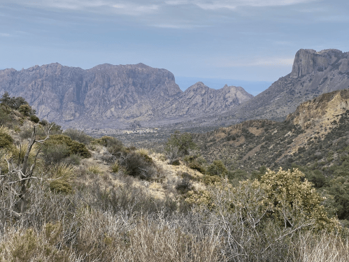 A scenic view of rugged mountains and valleys under a cloudy sky, showcasing diverse vegetation and rocky terrain.
