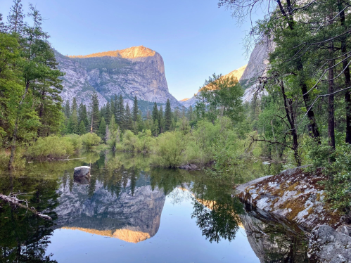 A serene mountain landscape with a calm lake reflecting trees and peaks under a clear blue sky.