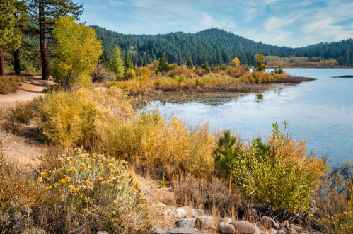 A serene lakeside scene with autumn foliage, surrounded by mountains and clear blue skies.