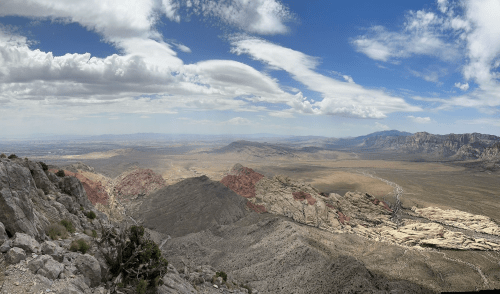 A panoramic view of rugged mountains and valleys under a partly cloudy sky, showcasing vast desert landscapes.