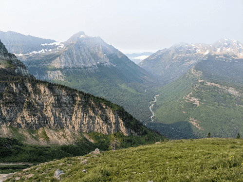 A panoramic view of a lush green valley surrounded by rugged mountains under a clear sky.