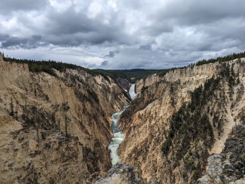 A dramatic canyon with steep cliffs and a river flowing through, under a cloudy sky in a natural landscape.