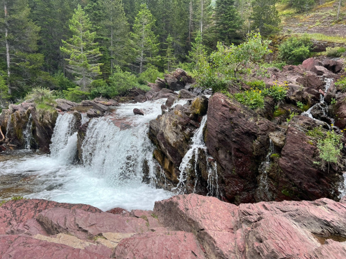 A serene waterfall cascading over rocky terrain, surrounded by lush green trees in a natural setting.