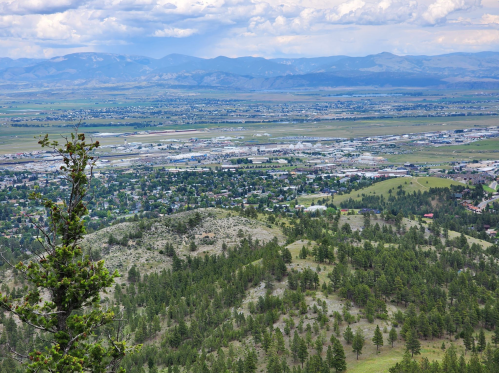 A panoramic view of a valley with a town, mountains in the background, and greenery in the foreground.