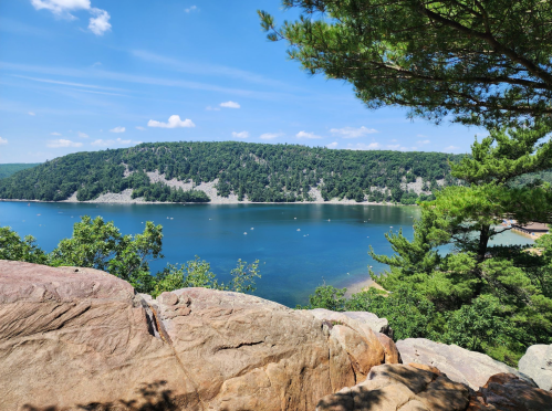 A scenic view of a calm lake surrounded by green hills and trees under a clear blue sky.