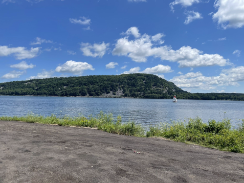 A serene lake scene with a green hill in the background, fluffy clouds in a blue sky, and a sailboat on the water.