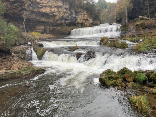 A serene waterfall cascading over rocky ledges, surrounded by lush greenery and autumn foliage.