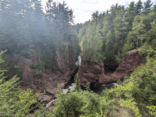 A scenic view of a river flowing through a rocky gorge, surrounded by lush green trees and a clear blue sky.