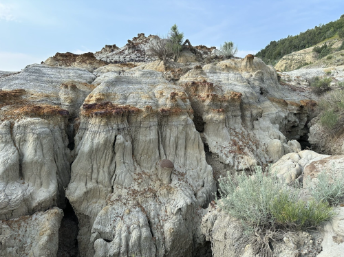 Rocky terrain with layered, weathered formations and sparse vegetation under a clear blue sky.